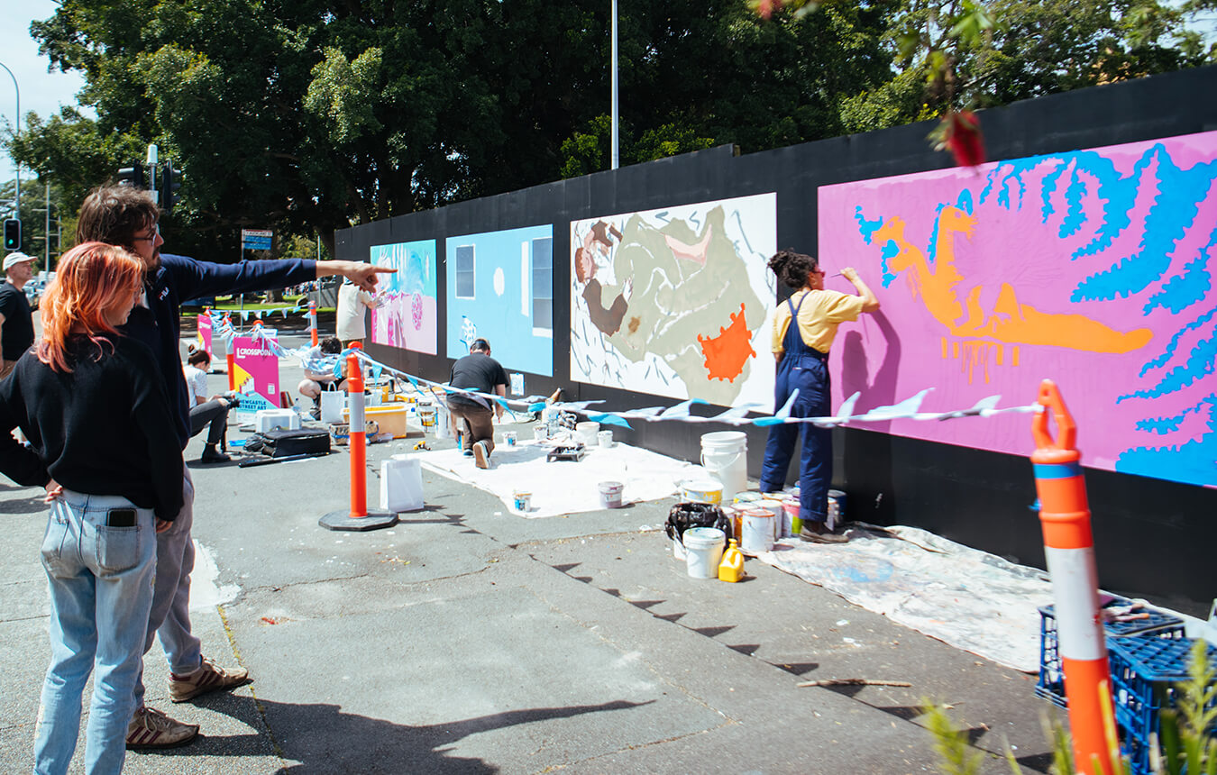 People watching artists paint murals for the Crosspoint Mentor Program on King Street, Newcastle