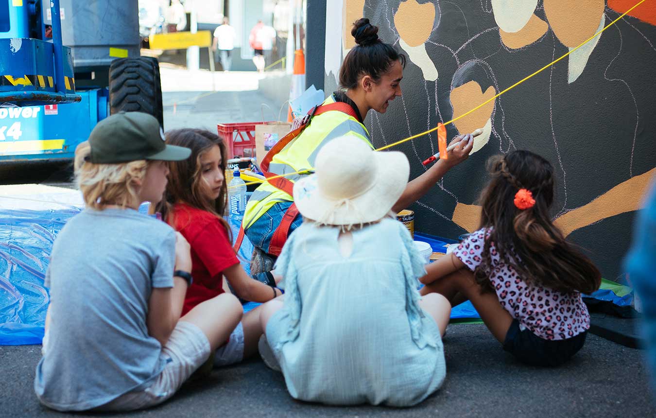 Children watching Jasmin Craciun paint a mural in Brown Street, Newcastle