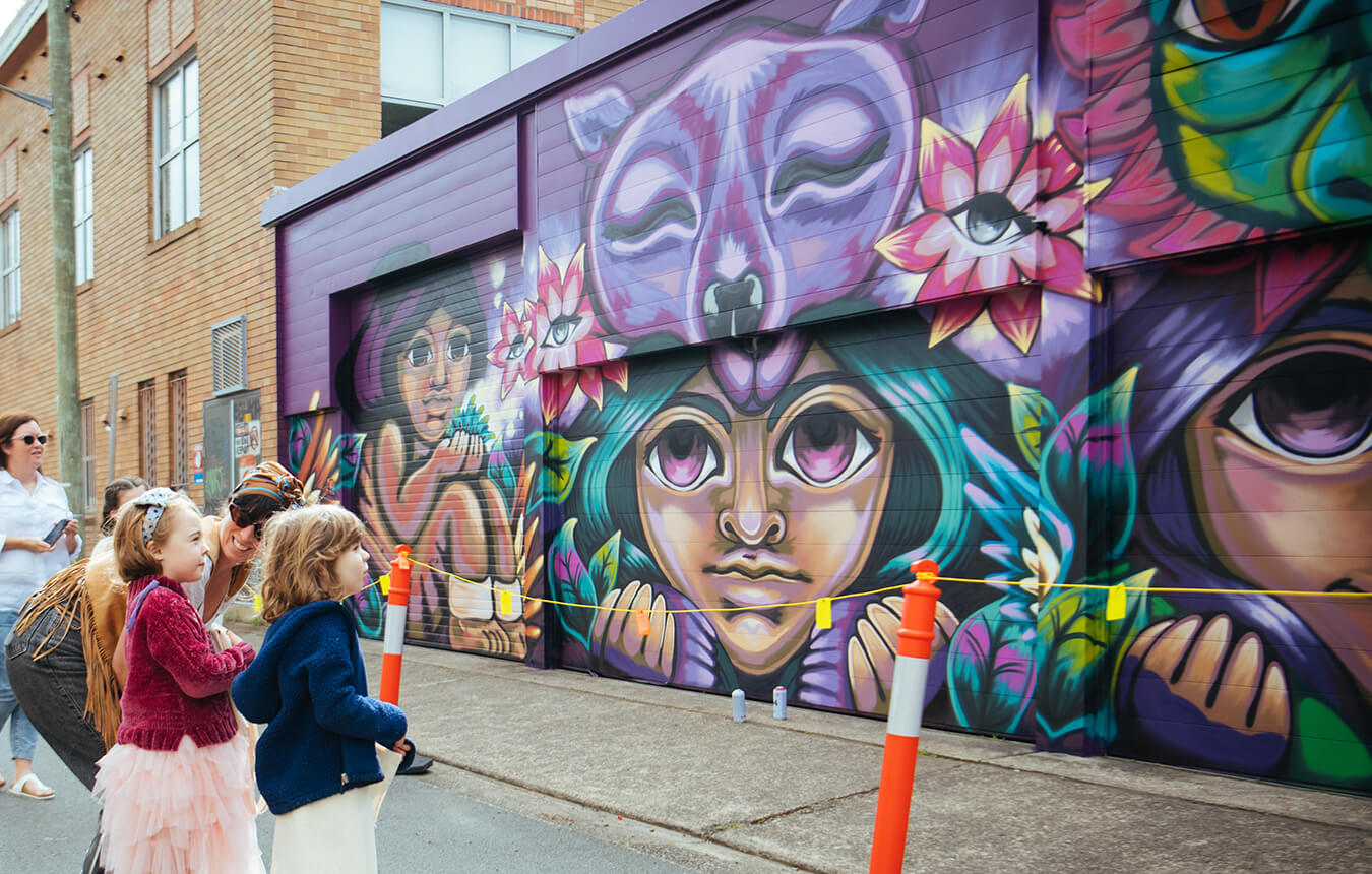 Adults and children looking at Goya Torres' mural in Gibson Street, Newcastle