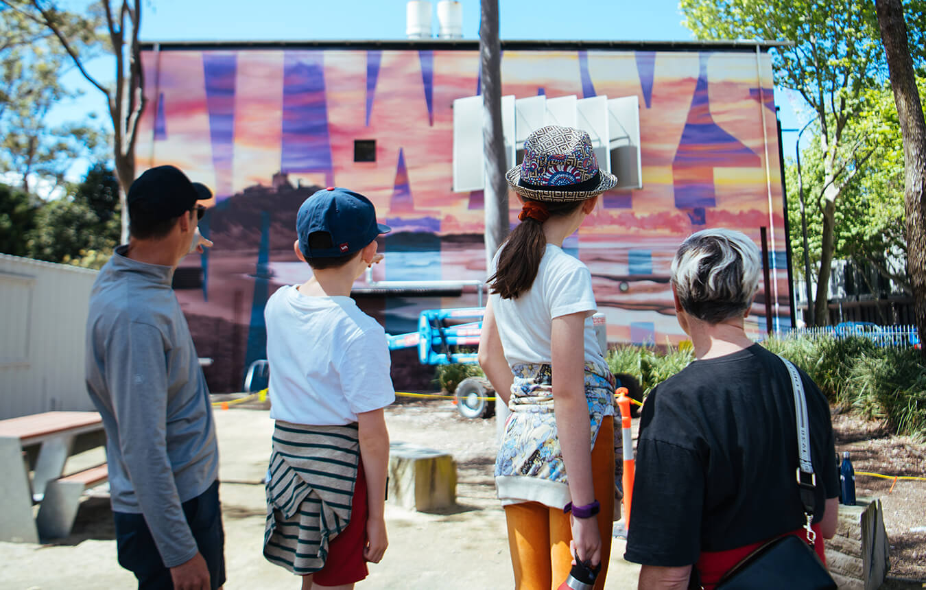 two adult and two children looking at the Damien Mitchell mural on TAFE Newcastle Art School buiding