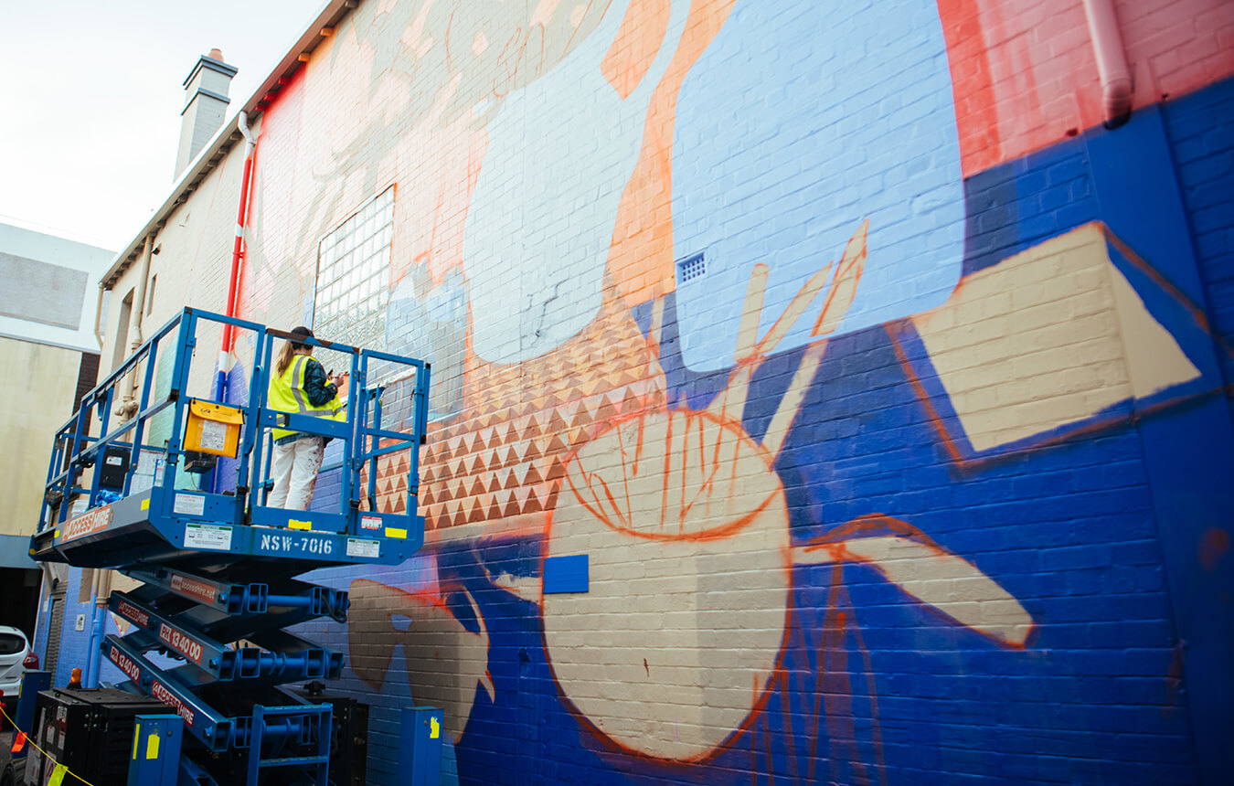 Claire Foxton on scissor lift in front of mural on Auckland Street laneway, Newcastle